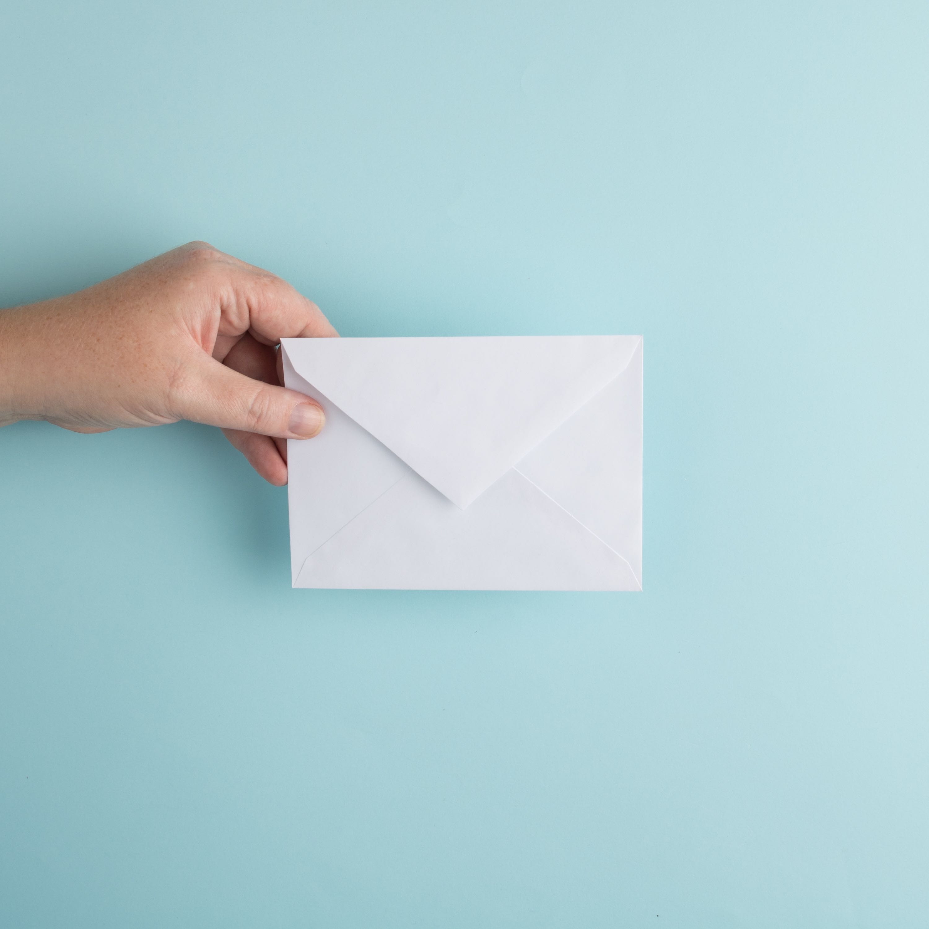 A hand holding a paper envelope over teal background